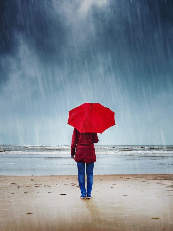girl with a red umbrella watching the sea in the rain, weather in andalucia in april